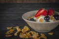 Yoghurt mix oatmeal, strawberry and grape topping in white bowl on the wood table with cornflakes placed in front of