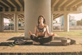 Yogi woman doing sitting in lotus position with a urban view under the bridge. Slim fit girl stretching outside on a sunset. Yoga Royalty Free Stock Photo