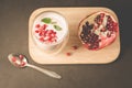 Yogurt. Yogurt with cereals, garnet and mint in glass and pomegranate fruit on a wooden tray. Dark backgtound table. Top view.