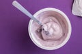 Yogurt cup with blue berry yoghurt, spoon and foil lid isolated on purple background Royalty Free Stock Photo