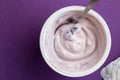 Yogurt cup with blue berry yoghurt, spoon and foil lid isolated on purple background - top view photograph Royalty Free Stock Photo