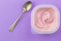 Yogurt cup with pink strawberry yogurt and small silver spoon isolated on purple background - top view photo of pink yoghurt Royalty Free Stock Photo