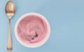 Yogurt cup with pink strawberry yoghurt isolated on baby blue background with copy space - selective focus image