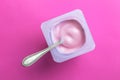 Yogurt cup with pink yoghurt and spoon on bright pink background