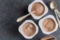 Yogurt cups with chocolate flavoured yoghurt on dark grey background with spoons - top view photo