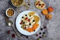 Yogurt with granola, berries and waffles on a white plate and nuts, peaches on a gray marble background. Healthy and