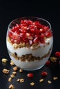 Yogurt with granola and pomegranate fruits in a glass cup on a black wooden table. Tasty dessert Healthy breakfast Royalty Free Stock Photo