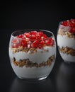 Yogurt with granola and pomegranate fruits in a glass cup on a black wooden table. Tasty dessert Healthy breakfast Royalty Free Stock Photo