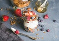 Yogurt oat granola with fresh berries, nuts, honey and mint leaves in glass jar on grey concrete textured backdrop Royalty Free Stock Photo