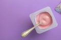 Yogurt in plastic cup with spoon - Top view of pink strawberry flavoured yoghurt on purple background Royalty Free Stock Photo