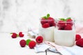 Yogurt with raspberries in jars, side view scene on a white marble background