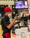Handsome barista waring a red hat and white masker making a cup of coffee