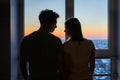 Yong couple in love standing close to window during the sunrise, silhouette medium shoot. Royalty Free Stock Photo