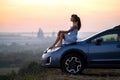 Yong happy female driver resting on hood of her car enjoying sunset view of summer nature. Travel destinations and recreation Royalty Free Stock Photo