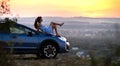 Yong happy female driver resting on hood of her car enjoying sunset view of summer nature. Travel destinations and recreation Royalty Free Stock Photo