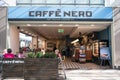 Exterior of Caffe Nero inside a shopping centre mall. Shows company logo, sign, branding and customers in seating area