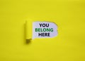 You belong here symbol. Concept words `You belong here` appearing behind torn yellow paper. Beautiful yellow background. Busines