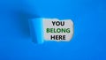 You belong here symbol. Concept words `You belong here` appearing behind torn blue paper. Beautiful background. Business and you