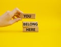 You belong here symbol. Wooden blocks with words You belong here. Beautiful yellow background. Businessman hand. Business and You