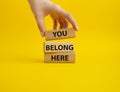 You belong here symbol. Wooden blocks with words You belong here. Beautiful yellow background. Businessman hand. Business and You