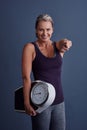 You can do it too. Studio portrait of an attractive mature woman holding a weightscale and pointing at the camera Royalty Free Stock Photo