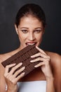 You can never have too much chocolate. Studio shot of an attractive young woman biting into a slab of chocolate.