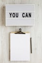 `You can` words on a lightbox, clipboard with blank sheet of paper on a white wooden background, top view. Overhead, from above, Royalty Free Stock Photo
