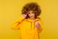 You are crazy! Portrait of curly-haired woman in urban style hoodie making stupid sign with finger near head