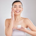 You dont need to use too much. a young woman applying a cream to her face against a grey background. Royalty Free Stock Photo