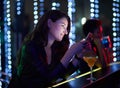 When are you getting to the club. a smiling young woman reading a text message while sitting at the bar in a nightclub. Royalty Free Stock Photo