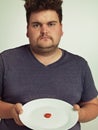 You have got to be kidding me. Portrait of an overweight man holding a plate with a tiny sliver of tomato.