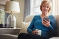 You have one new notification. a mature woman sitting on the sofa and using a mobile phone at home. Royalty Free Stock Photo