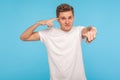 Are you idiot? Displeased man in t-shirt holding finger against his temple and pointing to camera, making crazy stupid gesture Royalty Free Stock Photo