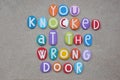 You knocked at the wrong door, creative text composed with multi colored stone letters over beach sand