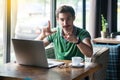 You are loser. Young serious businessman in green t-shirt sitting, pointing and showing loser gesture and looking at camera