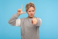 You are loser. Young woman with short curly hair in sweatshirt showing lame or loser gesture pointing to camera