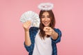 You may become rich! Portrait of happy lucky angelic girl with halo over head holding money and pointing to camera Royalty Free Stock Photo