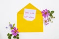 You are not alone message card handwriting in yellow envelope with pink flowers cosmos arrangement flat lay postcard