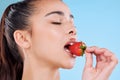When you snack, snack healthy. Studio shot of an attractive young woman biting into a strawberry against a blue