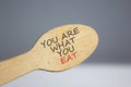 You are what you eat symbol. Wooden spoon on white background. Beautiful warm sunlight. Words `You are what you eat`. Beautiful