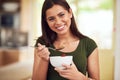 You are what you eat. Portrait of a happy young woman eating a bowl of muesli while standing in her kitchen. Royalty Free Stock Photo