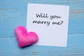 YOU WILL MARRY ME? word on paper note with pink heart shape decoration on blue wooden table background. Love, Wedding, Romantic