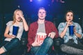 Youn man and women are sitting in chairs and watching movie. They are surprised and confused. Blonde girl put her hand Royalty Free Stock Photo