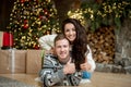 Yound couple beautiful wife hugging her beloved husband in room decorated for celebrating new year looking happy showing like sign