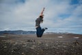 Yound woman jumping from joy on typical ring road view with empty road in the background without any cars in Iceland in summer,