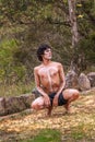 Young Aboriginal man squats in bird pose on grass in Newcastle, Australia