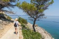 Young active feamle tourist wearing small backpack walking on coastal path among pine trees looking for remote cove to