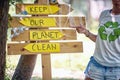 Young activist showing to wooden board saying, Keep our planet clean. Volunteers in nature picking up trash. Environmentalism,