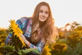 Young, adorable, energetic, female farmer posing next to a sunflower in the middle of a sunflower field during a golden sunrise Royalty Free Stock Photo