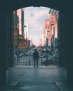 Young adult in an archway of a city alleyway, illuminated by the bright lights of a nearby street